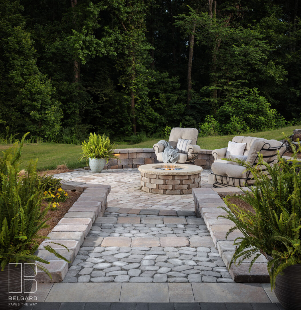 Cozy outdoor patio with cushioned chairs and a fire pit surrounded by lush greenery.